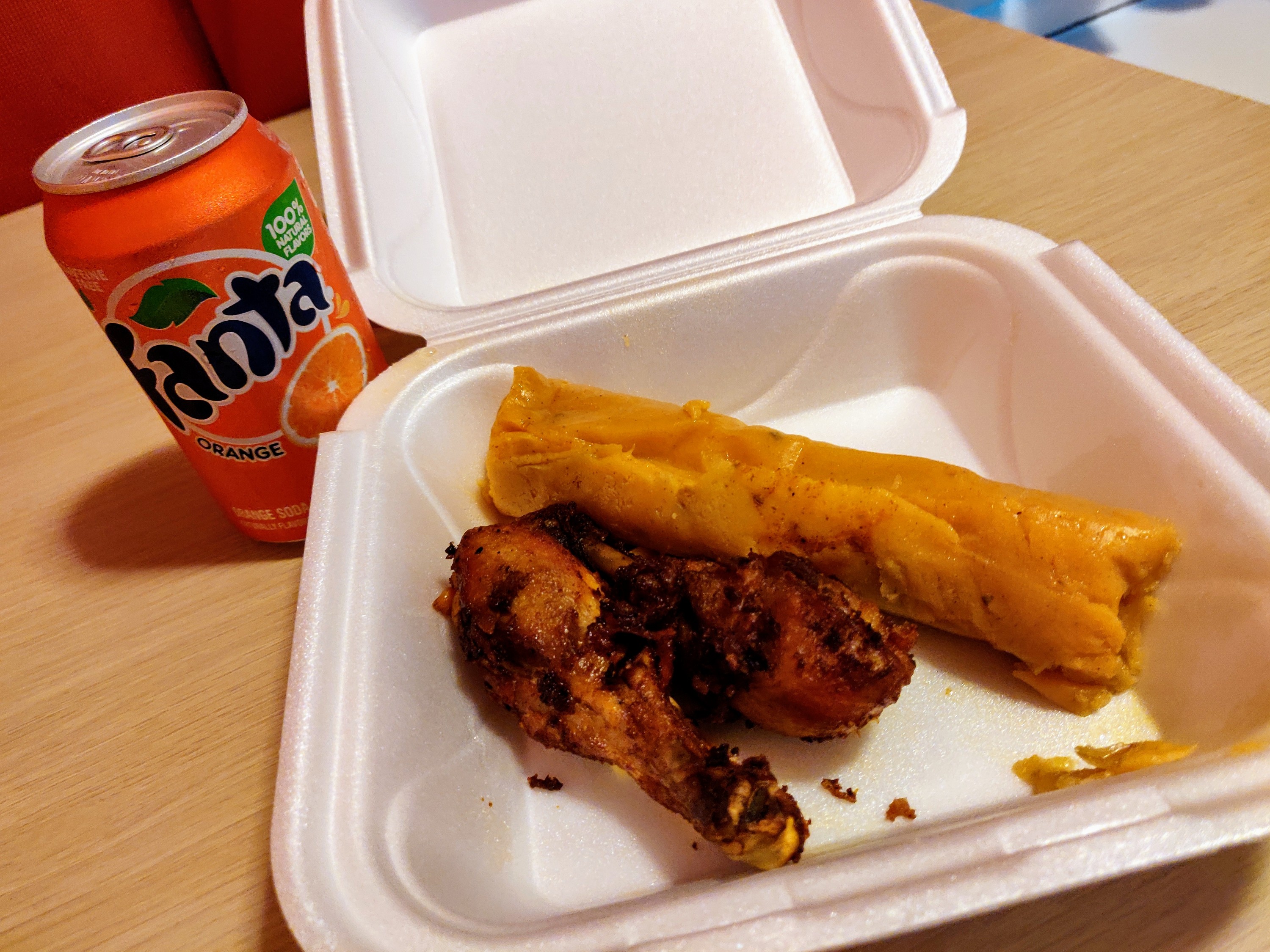 Open take out box showing a tamale, two chicken wings, can of Fanta orange to the side