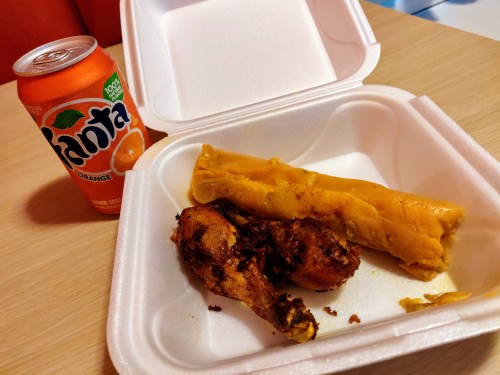 Open take out box showing a tamale, two chicken wings, can of Fanta orange to the side